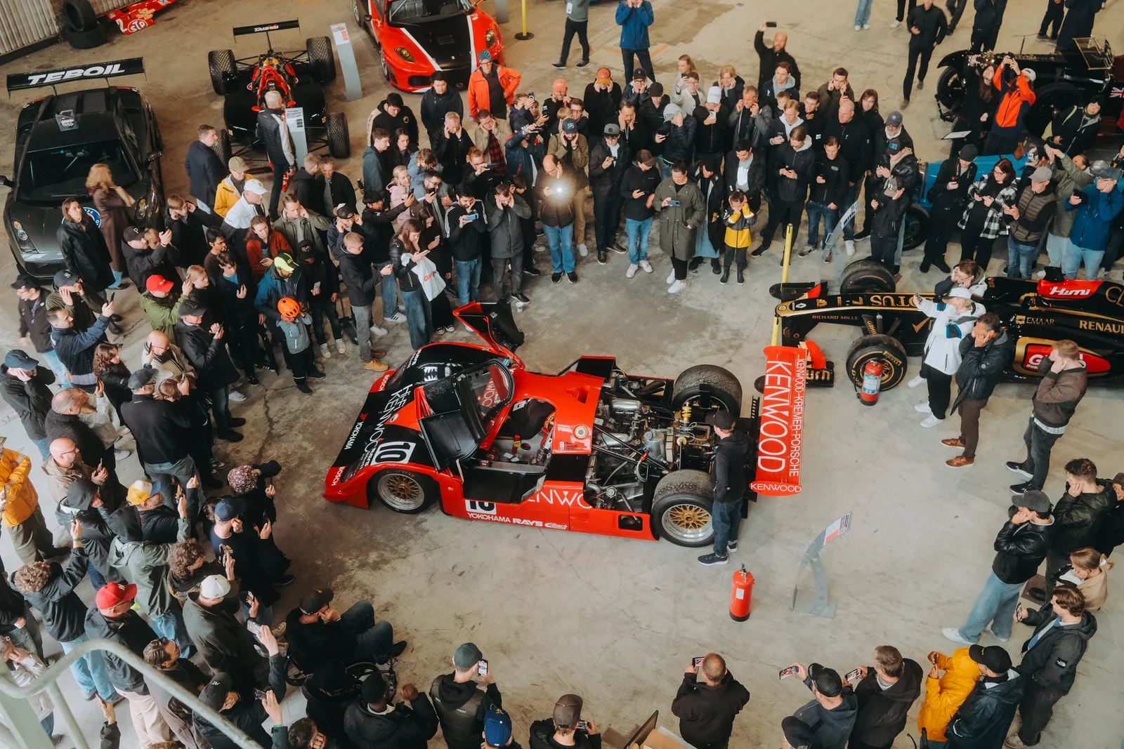 Publiken samlad runt en röd tävlingsbil i hallen på Gothenburg Classic Car Weekend, sedd uppifrån