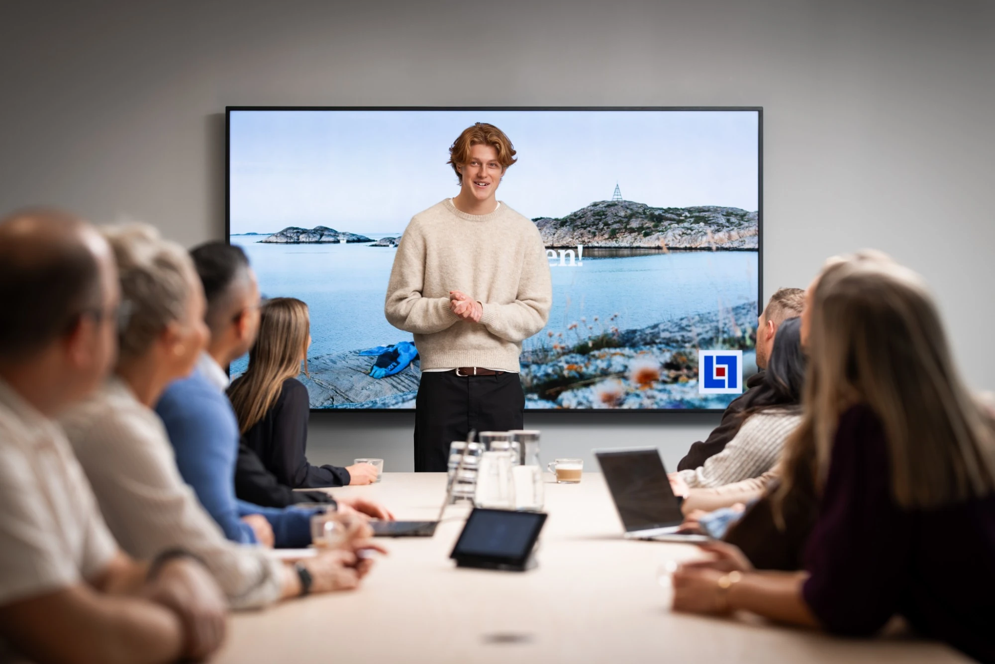 En medarbetare presenterar för kollegor runt ett konferensbord, Länsförsäkringars logotyp på skärmen bakom
